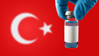 Vial of medicine being held against a backdrop of the Turkish flag